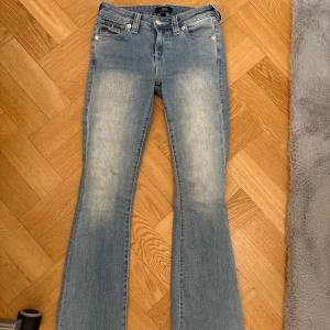 True Religion Becca Bootcut Jeans - Snygga ljusblå bootcut jeans från True Religion, modell Becca. Klassisk femficksdesign med silverfärgade knappar och detaljerad bakficka med logga. 