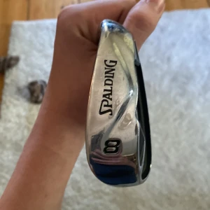 Spalding SP99 8 Iron Golfklubba - Spalding SP99 8-järn golfklubba i bra skick. Rostfritt stål, bekvämt grepp och snygg design. Passar både nybörjare och erfarna golfare. Mindre bruksspår men inga större defekter. Perfekt för dig som vill komplettera din golfutrustning.