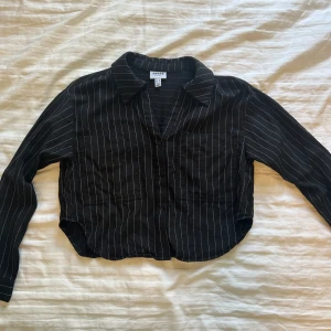 Svart randig skjorta från Aware XS - Svart skjorta från Aware by Vero Moda i storlek XS. Skjortan har vita tunna ränder, klassisk krage, två stora bröstfickor och lång ärm. Materialet är mjukt och lätt, perfekt för en chill och stilren look.