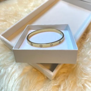 Guldfärgat armband med gravyr - Stilrent guldfärgat armband i rostfritt stål med rund form och ingraverade cirkelmotiv runt om. Armbandet är stelt och har en enkel, klassisk design som passar till många olika stilar. Perfekt accessoar för dig som gillar minimalistiska smycken.