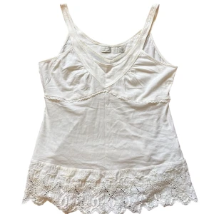 Vit linnetopp med spets från Zara - Supersöt vit linnetopp från Zara med smala axelband och v-ringning. Toppen har fina spetsdetaljer och broderier längst ner, vilket ger en romantisk vibe. Perfekt för varma dagar och enkel att styla med jeans eller kjol.