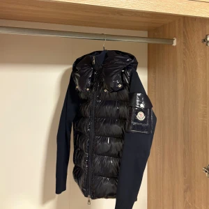 Moncler cardigan - Blå  - Säljer en Moncler Cardigan i färgen blå – en av Monclers mest populära modeller. Det är en hybrid mellan dunjacka och stickad cardigan, med dunfyllt nylon fram och stickade ärmar/rygg. Perfekt både som mellanlager på vintern eller som jacka på höst/vår.  - Äkta Moncler - Utrustad med NFC-chip för äkthetsverifiering - Dunfront som håller värmen utan att bli tung - Stickade ärmar och rygg för maximal komfort - Klassisk 2-vägs dragkedja fram - Storlek: XS - Skick: nästan helt ny, använd 5-7 gånger