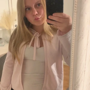 Ljusrosa kofta med knytband - Supersöt ljusrosa kofta med knytband i halsen. Koftan har en öppen front och långa ärmar, perfekt att slänga över ett linne eller t-shirt. Mjuk och skön känsla, passar till både jeans och kjol.