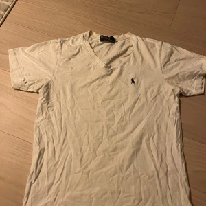 Vit v-ringad t-shirt från Polo - Vit t-shirt från Polo med v-ringning och klassisk broderad logga på bröstet. Tillverkad i 100% bomull och har korta ärmar. Enkel och stilren modell som passar perfekt till jeans eller shorts. Går väldigt enkelt att få bort skrynkligarna