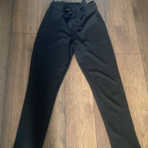 Svarta kostymbyxor med knytband - Stilrena svarta kostymbyxor med hög midja och knytband i midjan. Byxorna har raka ben, sidfickor och en mjuk, lite stretchig känsla. Perfekta för en clean och snygg look. Står ingen storlek men passar för xxs-xs. Pris kan diskuteras💕