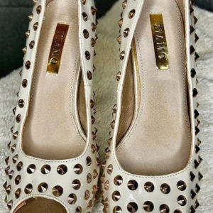  pumps med nitar från Tiamo - Klackskor från TIAMO, Storlek 37 Ett par vita/cremefärgade högklackade skor från tiamo med öppen tå och nitar. Knappt använda utan slitage beror på att dom legat i en låda tillsammans med andra skor. 