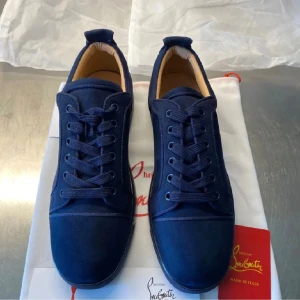 Mörkblå sneakers från Christian Louboutin - Snygga mörkblå sneakers från Christian Louboutin i mocka med klassisk röd sula. Skorna har rund tå, platt sula och snörning. Insidan är ljusbeige och de levereras med originalpåse och box. Perfekta för dig som vill sticka ut med exklusiva detaljer. Har kvitto, allt tillkommer!