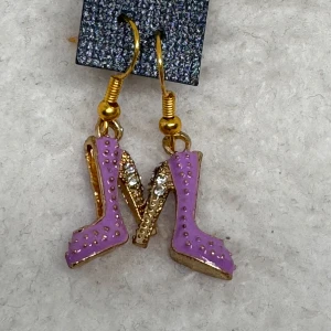 Lila örhängen med stilettklackar - Unika örhängen i form av lila stilettklackar med gulddetaljer och små glittriga stenar. Perfekt accessoar för dig som vill sticka ut och addera en lekfull touch till din stil. Krokarna är i sterling silver . Nya