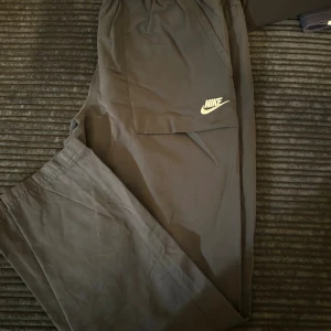 Svarta mjukisbyxor från Nike - Svarta mjukisbyxor från Nike med klassisk logga på benet. Byxorna har elastisk midja och raka ben, perfekta för chill eller träning. Tillverkade i mjukt material som känns skönt mot huden.