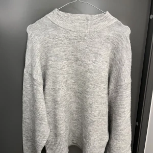 Grå stickad tröja från H&M - Mysig grå stickad tröja från H&M i storlek XS. Tröjan har en hög ribbad halsringning, långa ärmar och breda ribbade muddar vid ärmslut och nederkant. 🤎