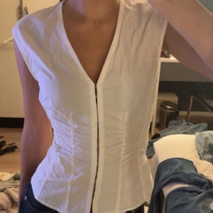 Vit ärmlös skjorta med v-ringning - Säljer en vit skjorta från Weekday med djup v-ringning och figurnära passform!