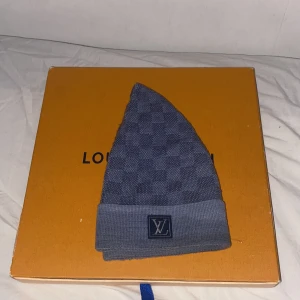 Light blue Louis Vuitton mössa med rutmönster - Snygg blå mössa från Louis Vuitton med diskret rutmönster och uppvikt kant. LV-logga framtill ger en lyxig touch. Stickad i mjukt material som håller dig varm och stilren. Perfekt accessoar för dig som vill ha designer vibes i vinter. Sällsynt modell. Priset kan diskuteras.