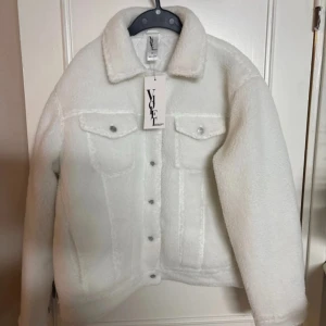 Vit teddyjacka från Violet Romance - Supermjuk och fluffig vit teddyjacka från Violet Romance. Jackan har klassisk krage, två bröstfickor med lock och knappar framtill. Perfekt för dig som vill ha en mysig och trendig look med oversized känsla.