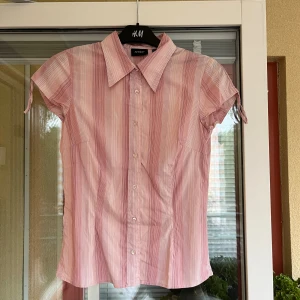 Rosa skjorta från InWear - Säljer en skjorta från InWear med ljusrosa och vita ränder. Skjortan har klassisk krage, korta ärmar och knäppning framtill med vita knappar. Storlek 32.