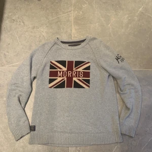 Morris tröja – Medium - Snygg och tidlös stickad tröja från Morris i storlek Medium. Grå bas med klassiskt brittiskt Union Jack-inspirerat motiv framtill och broderad logga på ärmen. Mjuk och bekväm kvalitet, perfekt för både vardag och mer uppklädda tillfällen.  🔹 Färg: Grå med rött, vitt & svart tryck 🔹 Storlek: Medium (normal i passformen) 🔹 Märke: Morris – för gentlemen 🔹 Skick: Mycket bra, sparsamt använd  💰 Pris: 750 kr