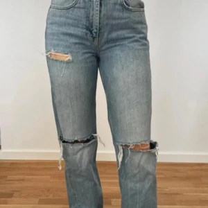 Blåa raka jeans med slitningar - Snygga blå jeans från Gina Tricot med hög midja och raka ben. Jeansen har slitna detaljer vid knäna och på bakfickan för en trendig look. Klassisk femficksmodell i denim med dragkedja och knapp framtill.