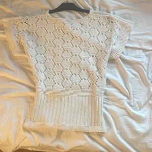 Vit stickad topp med hålmönster - Säljer en vit stickad topp med korta ärmar och snyggt hålmönster i geometriskt mönster. Toppen har bred ribbad nederkant och är perfekt för dig som gillar en luftig och stilren look. Passar till både jeans och kjol för en fräsch vibe.