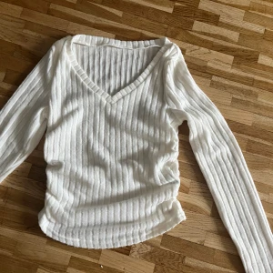 Vit ribbad långärmad tröja - Säljer en vit långärmad tröja med v-ringning och ribbat mönster. Tröjan är mjuk och stretchig, perfekt för lager-på-lager och passar till både jeans och kjol. Enkel och stilren design som funkar året runt. Är dock lite genomskinlig