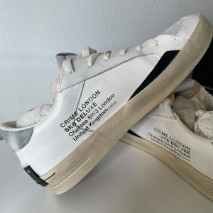 Crime London Skate Deluxe sneakers - Snygga Skate Deluxe sneakers från Crime London i vitt skinn med grå mockadetaljer och svarta inslag. Skorna har rund tå, snörning och en beige sula som ger en cool vintage vibe. Perfekta för dig som gillar streetstyle och unika detaljer. Priset går alltid att diskutera har du en fråga det är ba o skriva 