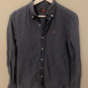 Mörkblå skjorta från Morris - Snygg mörkblå skjorta från Morris med klassisk krage och knappar framtill. Skjortan är långärmad och tillverkad i mjuk bomull, perfekt för dig som gillar stilrena plagg med diskreta detaljer. (TYVÄRR har den fläckar under armarna, men kan förhoppningvis gå att lösa!) 