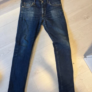 Mörkblå jeans från J.Lindeberg - Snygga mörkblå jeans från J.Lindeberg med klassisk femficksdesign och diskreta slitningar. Jeansen har slim passform, tillverkade i mjukt denimtyg med detaljer i kontrastsömmar och läderpatch bak i midjan. 34-34 sitter som 30-32