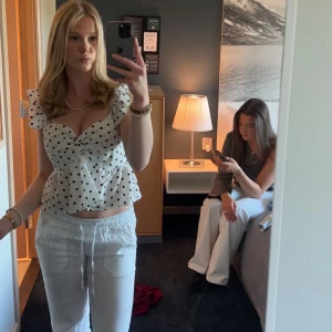 Vit prickig blus med volangärmar - Supersöt vit blus med svarta prickar, volangärmar och twistad omlott framtill. Blusen har smockad rygg och lätt utsvängd nederdel. Perfekt för dig som gillar lekfulla detaljer och trendiga mönster.Strl S men passar XS🤍