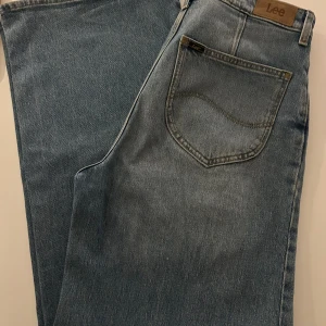 Lee Stella A Line blå jeans W30 L33 - Snygga blå jeans från Lee, modell Stella A Line. Klassisk femficksdesign med Lee-logga på bakfickan och läderpatch i midjan. Jeansen har rak passform och är tillverkade i slitstarkt bomullsmaterial. Perfekt för dig som gillar tidlös denimstil.