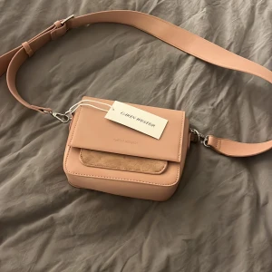 Rosa väska - Ljusrosa väska aldrig använd med lappen kvar. Nypris 499. Väskan har ett lock med magnetknäppning, en ficka framtill med mockadetalj och ett rymligt huvudfack med innerficka med dragkedja. 
