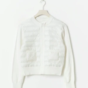 Vit rib kofta med dragkedja - Säljer en vit quiltad kofta med dragkedja framtill och två fickor. Tröjan har ribbade muddar, lång ärm och en croppad passform. Framsidan är vadderad och ger en snygg kontrast till de stickade ärmarna och ryggen. Perfekt för lager-på-lager-stil.