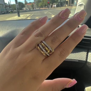 Unik länkad ring i guld och silver - Säljer en cool och unik ring med fyra sammanlänkade ringar i guld och silver. Två av ringarna är dekorerade med glittrande stenar, vilket ger extra bling. Designen är modern och sticker ut, perfekt för dig som gillar statement-smycken. Ringarna är i rostfritt stål med guldplätering. Skickar med en söt liten smyckespåse😊 Endast testad på då storleken var liten på mig!!  Omkrets: ca 57,1 mm Diameter: 18,1 mm  EU-storlek: 57-58 mm  US-storlek: 8   #ring #smycke #statementring #guldochsilver #bling 