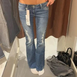 Bootcut lågmidjade jeans  - Snygga blå bootcut jeans med slitna detaljer framtill och klassiska fickor bak med knapp. Jeansen har låg midja och i storlek Xs.❤️