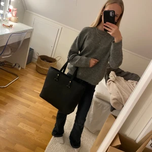 Svart axelväska i skinnimitation - Fin stor och svart handväska i skinnimitation. Smidig och rymmer bra plats åt exempelvis dator eller mappar. Funkar att ha på både armen och axeln. 2 fickor på insidan av väskan som rymmer mobil, laddare eller exempelvis pennor.