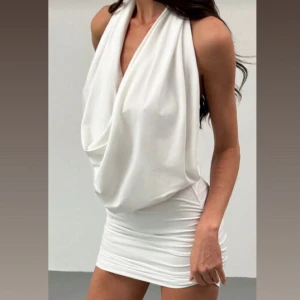 Vit kort klänning med öppen rygg - Supersnygg vit kort klänning med draperad omlottfront och djup urringning. Klänningen har en tight passform över höften och en helt öppen rygg som ger en riktigt cool look. Aldrig använd och i topp skick! 