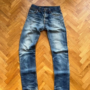 Nudie Jeans Steady Eddie Dry - Modell Steady Eddie Org Tonal Dry (Blåa detaljer på backfickan). Köpta ca 2010 i butik och använda väl (15+ år!). Har lagats flera gånger i butik. Väldigt fina fades och slitningar  W30/L36 Yb-längd 110cm Ib -längd 80cm Benöppning 17cm Midja 39cm Lår 25,5cm  Skicka DM för fler bilder/funderingar.