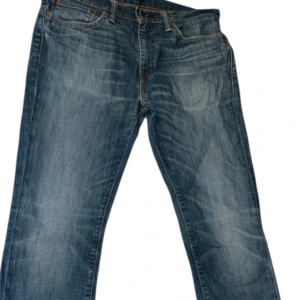 Levi's 511 blå jeans straight fit - Snygga blå Levi's 511 jeans med klassisk femficksdesign och ikonisk röd Levi's-tag på bakfickan. Jeansen har en rak passform och subtila slitningar för en cool, avslappnad look. Tillverkade i mjukt denim med orange kontrastsömmar.