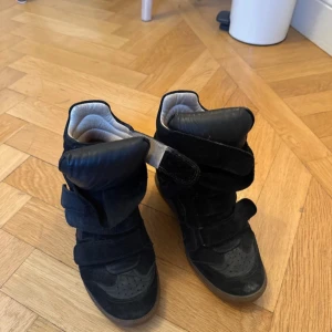 Svarta Isabel Marant wedge sneakers - Säljer ett par svarta wedge sneakers från Isabel Marant med högt skaft och breda kardborreband. Skorna är i mocka och skinn, har rund tå och en diskret plattformssula. Insidan är ljusbeige och de har en riktigt cool streetstil.