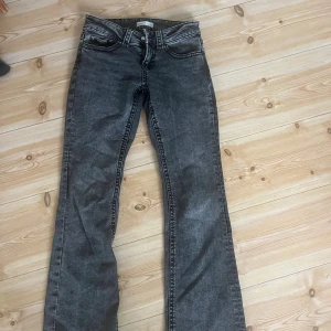 Mörkgråa bootcut jeans från Gina Tricot - Snygga svarta jeans från Gina Tricot i storlek 34. Modellen har bootcut-ben och klassisk femficksdesign med markerade sömmar och knappar på bakfickorna. Jeansen har normal passform och är tillverkade i jeansmaterial med en mörk tvätt. Säljer då dom är lite för korta för sig som är 171cm. Inga defekter.