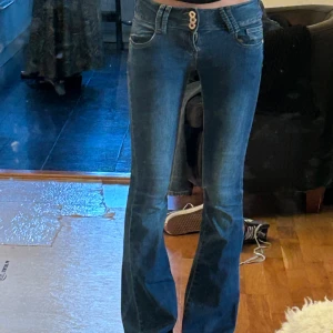Blå low waist bootcut jeans med dubbla knappar - Snygga blå bootcut jeans med dubbla knappar i midjan och klassiska fickor både fram och bak. Jeansen har en låg midja och är tillverkade i stretchigt denimtyg som sitter skönt. Perfekta för dig som gillar en retroinspirerad look. Super snygga o e super low waist. Perfect för hösten🍂passar xs o s
