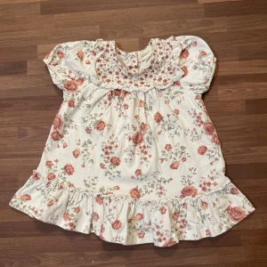 Blommig klänning - Sparsamt använd utan anmärkningar. Blommig klänning från Newbie stl 62 (2-4mån). Söta volangdetaljer med knappar bak.