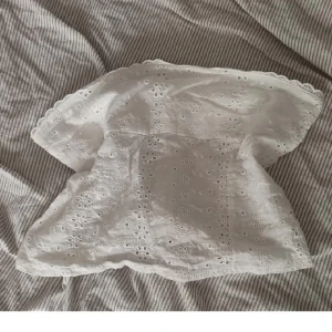 Vit broderad tubtopp med spetskant - Söt vit tubtopp med broderade blommor och hålmönster. Toppen har en romantisk känsla med spetskant upptill och nertill. Perfekt för varma dagar och enkel att matcha med jeans eller kjol.