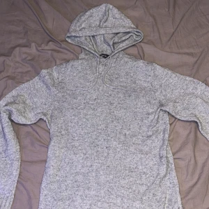Grå stickad hoodie med huva - Mysig grå stickad hoodie med huva och snörning. Tröjan har långa ärmar och ribbade muddar vid ärmslut och nederkant. Perfekt för kyliga dagar när du vill vara både bekväm och snygg. Storlek S men passar även M.