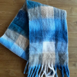 Rutig ullhalsduk - Mysig och fluffig halsduk med rutigt mönster i olika nyanser av blått, beige och vitt (liknar acne studios). Halsduken har långa fransar i ändarna och är tillverkad i mjuk ull, perfekt för kalla dagar. Halsduken är 240cm lång och 40cm bred 