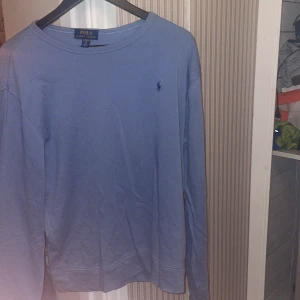 Ljusblå tröja från Polo Ralph Lauren - Säljer en stilren ljusblå tröja från Polo Ralph Lauren med klassisk rund halsringning och broderad logga på bröstet. Tröjan är långärmad och tillverkad i mjuk bomull, perfekt för en clean och avslappnad look. Skicket är 10/10 