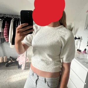 Vit croppad tröja med puffärm - Säljer en söt vit croppad tröja  med korta puffärmar och rund hals. Toppen har en lätt textur i materialet och sitter snyggt med en normal passform. Perfekt att styla med jeans eller kjol för en fräsch look.