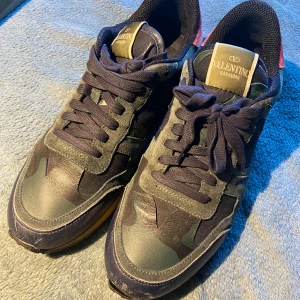 Valentino Rockrunner sneakers camouflage - Snygga Valentino Rockrunner sneakers i mörkblått och grönt med camouflage-mönster. Skorna har detaljer i mocka och skinn, klassisk snörning och coola nitar på hälen. Perfekta för dig som vill sticka ut med exklusiva och trendiga sneakers.