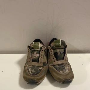 Valentino Rockrunner sneakers camouflage - Säljer ett par Valentino Rockrunner sneakers med grymt coolt camouflage-mönster i grönt, beige och brunt. Skorna har detaljer i mocka och skinn, svart innersida och röd häl. Platt sula och snörning framtill. Perfekt för dig som gillar streetstyle och designer. Snören fins!!