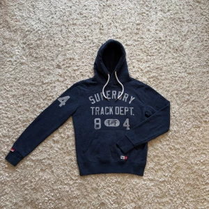 Mörkblå hoodie från superdry - Riktigt snygg o unik blå hoodie från superdry i storlek S. Den är i bra skick men lite nopprig på vissa stället. Tveka inte på o skriva vid fler frågor!