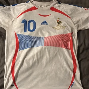  Zidane VM 2006 fotbollströja - Säljer en vit Frankrike t shirt från Adidas med blå och röda detaljer. Tröjan har korta ärmar och nummer 10 på framsidan samt namnet 'Zidane' på baksidan. Från final 2006 Italien vs Frankrike. LIMITED EDITION! Haft den bara hängd uppe i rummet. Först till kvarn!