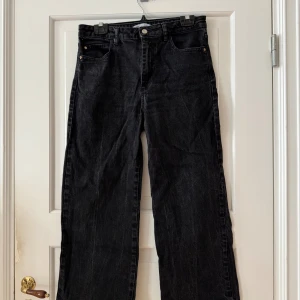 Svarta wide jeans från Zara, stl 42 - Svarta jeans från Zara i storlek 42 med klassisk femficksmodell och raka, vida ben. Jeansen har hög midja och är tillverkade i kraftigt denimtyg med snygga silvriga nitar och knapp. Perfekta för en avslappnad och trendig look. Använda men i fint skick. Ankellånga. 
