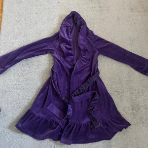 Lila morgonrock från Gina Tricot - Säljer en lila morgonrock i mjuk sammet från Gina Tricot. Jackan har volangkant nertill, lång ärm, huva och knytskärp i midjan. Perfekt för dig som vill ha något skönt på morgonen eller efter duschen. Säljer pågrund av att den är för liten för mig.